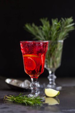 Biberiye karanlık bir arka plan üzerinde bir arka plan üzerine kireç, biberiye ve buz küpleri ile kırmızı renk bir kokteyl ile bir bardak
