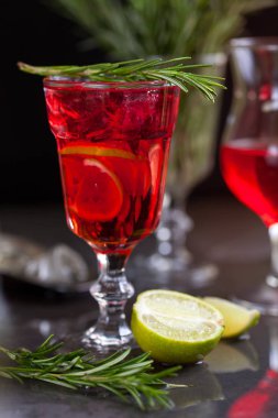 Biberiye karanlık bir arka plan üzerinde bir arka plan üzerine kireç, biberiye ve buz küpleri ile kırmızı renk bir kokteyl ile bir bardak