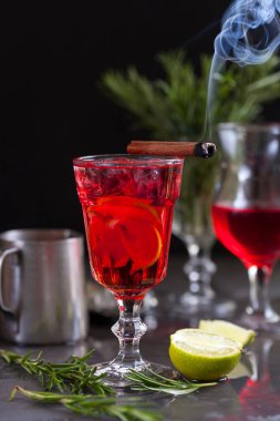 kireç, kırmızı meyveler, biberiye, biberiye karanlık bir arka plan üzerinde bir arka plan üzerine tarçın ve buz küpleri yanan kırmızı renk bir kokteyl ile bir bardak