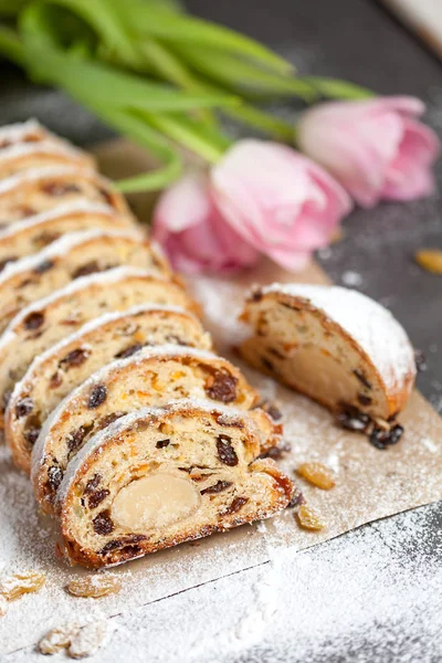 Bolo recém-assado com doces, passas e frutas cristalizadas, polvilhado com açúcar em pó em uma mesa cinza com tulipas rosa Fotografias De Stock Royalty-Free