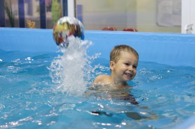 Mutlu küçük çocuk havuzda top oynuyor.