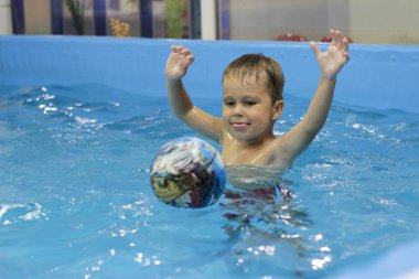 Yüzme havuzunda top oynamaktan mutlu küçük çocuk