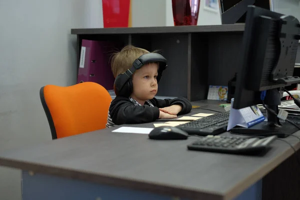 Jongetje met koptelefoon zit op computer in kantoor — Stockfoto