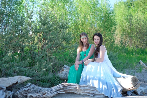 Duas raparigas estão sentadas num tronco junto ao mar. — Fotografia de Stock