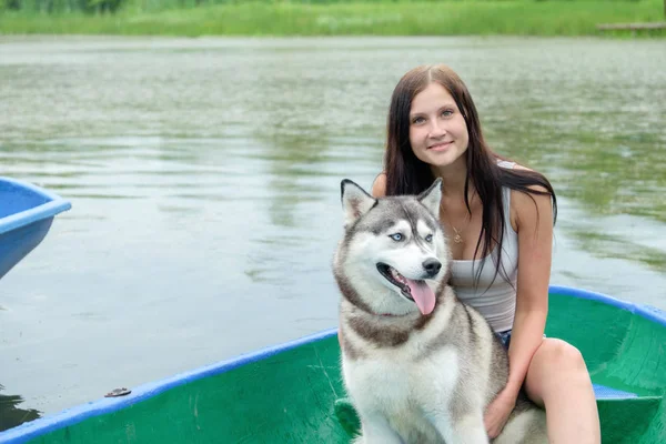 Chica joven y su perro husky está sentado en un parque cerca del lago en verano —  Fotos de Stock