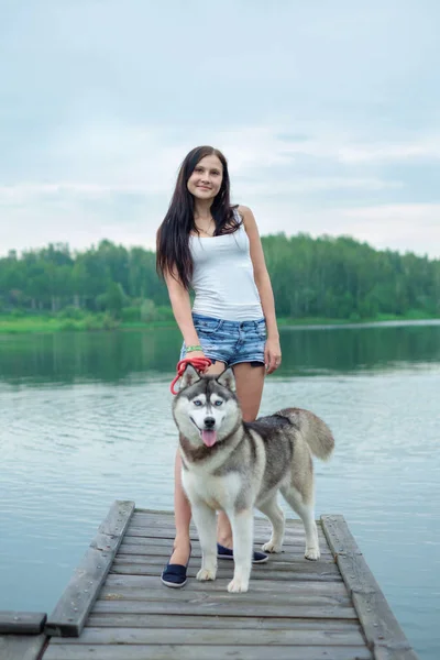 Unga kvinnor och hennes hund husky sitter i en park nära sjön i sommar — Stockfoto