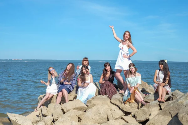 Zespół lub Grupa dużo pięknych młodych kobiet młodych dorosłych stanąć na kamienie na plaży podczas przytrzymaj przezroczystego szkła ze świeżych pomarańczy napojów bezalkoholowych koktajl. Na imprezie — Zdjęcie stockowe