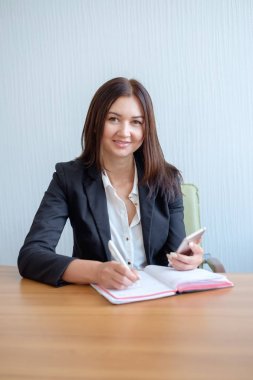 Güzel genç kadın bir akıllı telefon kullanarak ve masa başında otururken notlar yapma