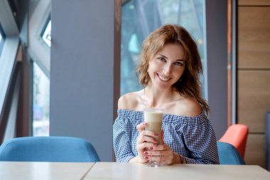 Bir fincan kahve latte ile bir kafede oturan genç ve güzel kadın