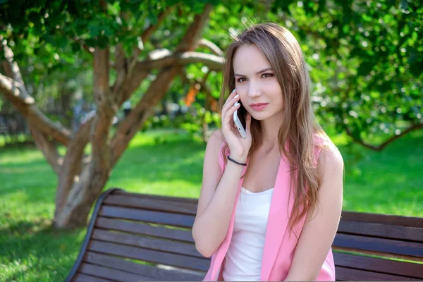 Happy roztomilá mladá žena usměje a mluví o telefonu v parku — Stock fotografie