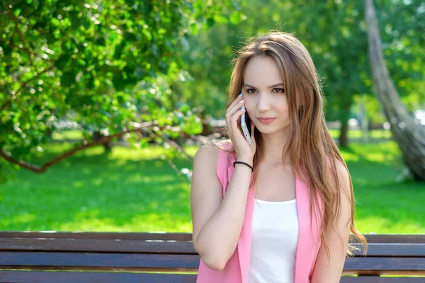 Happy cute młoda kobieta uśmiecha się i rozmawia przez telefon, w parku — Zdjęcie stockowe