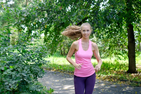 Güneşli yaz gününde yeşil parkta koşan güzel genç bir kadın.