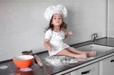 Sevimli küçük kız önlük ve Şef şapkalı hamur yoğurma ve pişirme sırasında gülümseyen