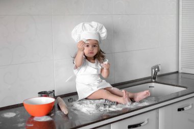 Küçük gülümseyen bebek kız baker beyaz aşçı şapkası ve önlük tle mutfak bir hamur kneads
