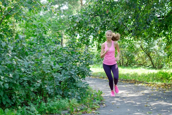 Uma mulher a correr pela estrada do parque primaveril. Treino num parque. Menina bonita ajuste. Modelo de fitness ao ar livre . — Fotografia de Stock