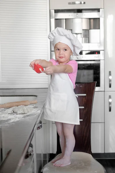 Küçük gülümseyen bebek kız baker beyaz aşçı şapkası ve önlük tle mutfak bir hamur kneads — Stok fotoğraf