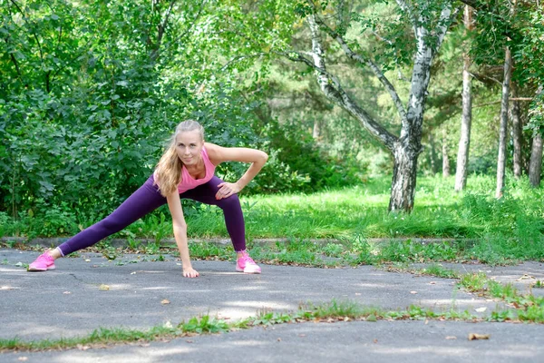 Porträtt av sportig kvinna göra stretchingövningar i parken innan träning. Kvinnliga idrottare förbereder för jogging utomhus. Löpare gör sida utfall. Sport active livsstilskoncept. med kopia utrymme — Stockfoto