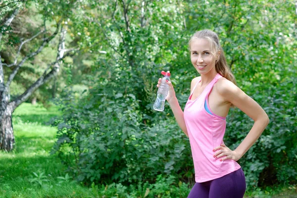 Jolie jeune sportive a terminé son travail et maintenant boire de l'eau et sourire dans le parc — Photo