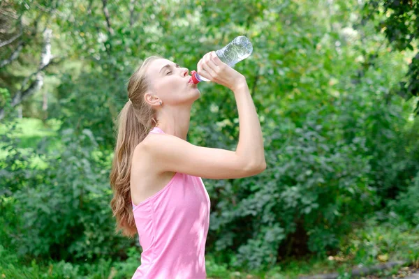 Atractiva joven deportista terminó su trabajo y ahora beber agua y sonreír en el parque — Foto de Stock