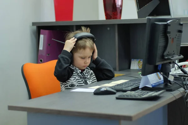 Jongetje met koptelefoon zit op computer in kantoor — Stockfoto