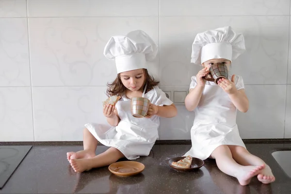 Две маленькие пекари пьют чай с пирожными на кухне. — стоковое фото