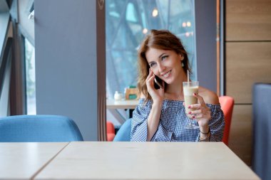 Mutlu kadın cep telefonu üzerinde modern kahve dükkanı iç tek başına otururken arkadaşıyla konuşurken