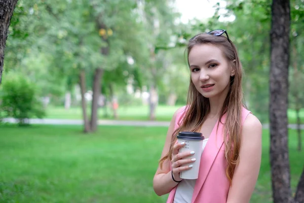 Portret piękne dziewczyny spacerują po parku. Utrzymanie Fast drink w jednej ręce. — Zdjęcie stockowe