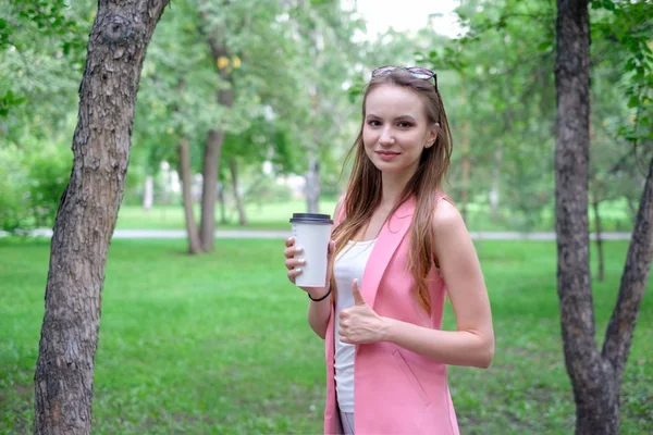 Portret piękne dziewczyny spacerują po parku. Utrzymanie Fast drink w jednej ręce. — Zdjęcie stockowe