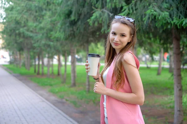 Retrato de una hermosa chica caminando por el parque. Mantener la bebida para llevar en una mano . — Foto de Stock