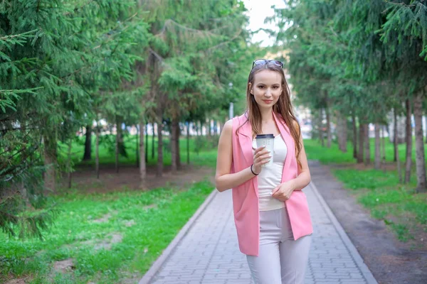 Retrato de menina bonita andando no parque. Mantendo a bebida takeaway em uma mão . — Fotografia de Stock
