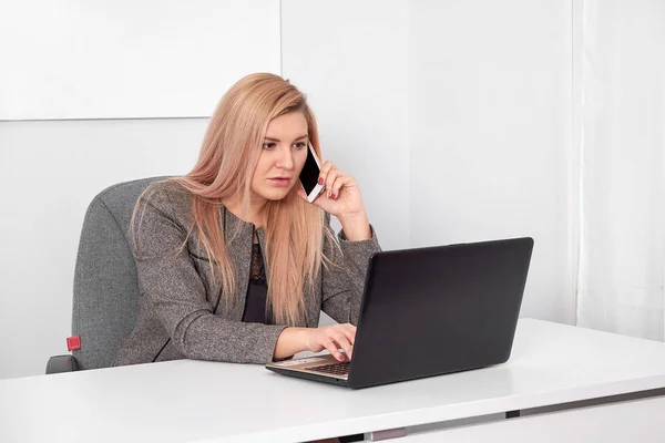 Zár-megjelöl-ból egy érdekelt üzletasszony munka az irodájába, fehér öltönyt. Ő beszél a telefonon, és dolgozik-val laptop — Stock Fotó