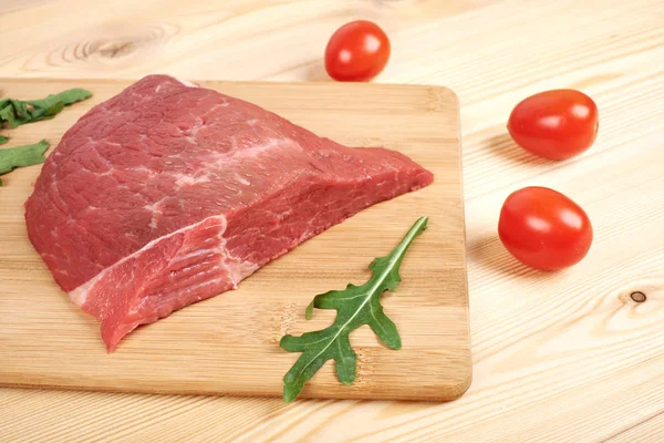 Rått nötkött på skärbräda med grönsaker på en trä bakgrund — Stockfoto