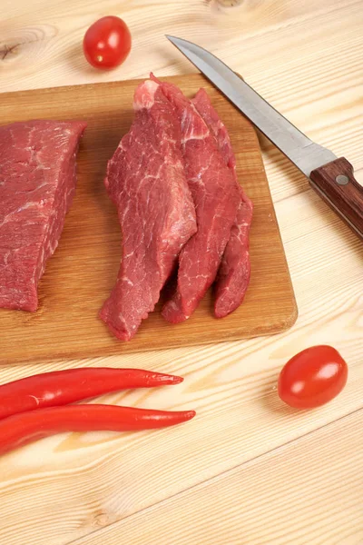 Carne de bovino em bruto cortada sobre tábua de corte e produtos hortícolas — Fotografia de Stock