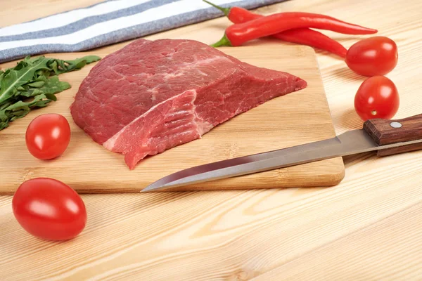 Raw beef meat on cutting board with vegetables on a wooden background Stock Image