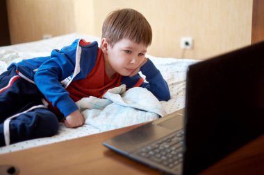 Genç çocuk evde bir yatak odasında bir dizüstü bilgisayar kullanarak