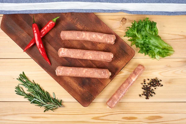 Raw sausages with vegetables and spices on wooden background — Stock Photo, Image