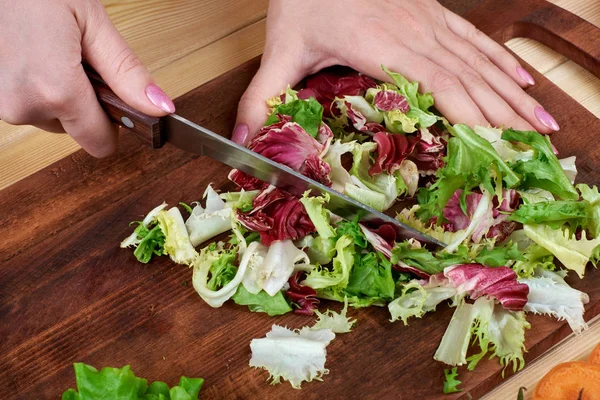 Frauenhände hacken grünen Salat, kochen Gemüsesalat auf hölzernem Hintergrund — Stockfoto