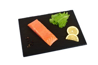 Somon filetosu ve siyah şist tahtasında küçük dilimler, limon ve salata ile birlikte. beyaz arkaplan