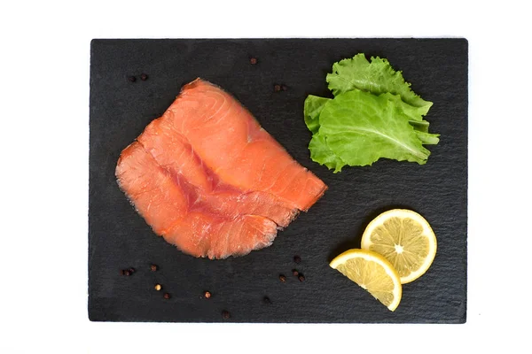 Tři plátky lososa na černé břidlicové desce s citronem a salátem. Na bílém pozadí — Stock fotografie