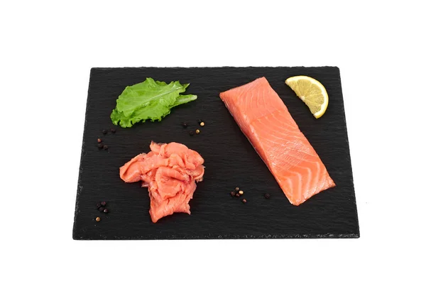 Sliced salmon fillet on the black shale board, with lemon and salad. On white background — Stock Photo, Image