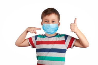 Tıbbi maske takan genç bir çocuk başparmağını kaldırmış ve maskeyi işaret ediyor. Tıbbi maske takmak iyidir. corona virüsü konsepti.