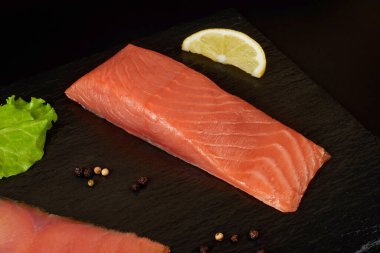 Siyah şist tahtasında dilimlenmiş somon filetosu, limon ve salata. Beyaz arkaplanda