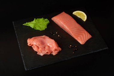 Siyah şist tahtasında dilimlenmiş somon filetosu, limon ve salata. Beyaz arkaplanda