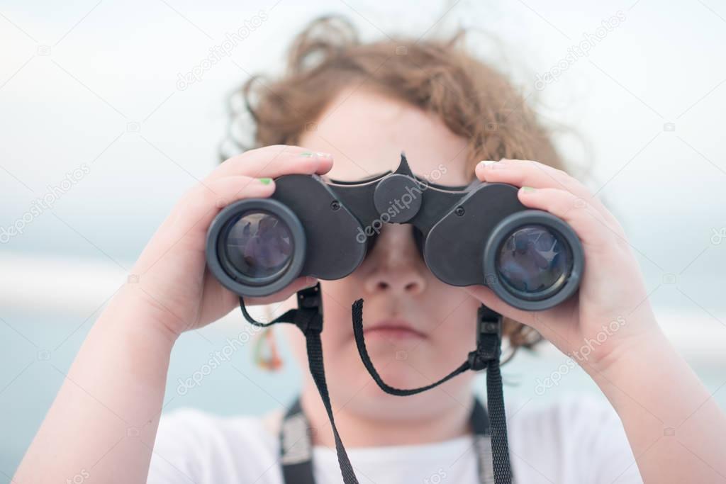 Beautiful young girl on boat looking directly at camera through binoculars