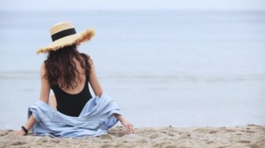 Plajda oturan şapkalı kız.