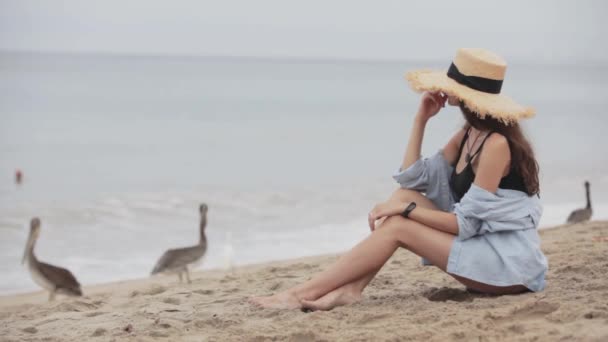 Mädchen mit Hut sitzt am Strand — Stockvideo