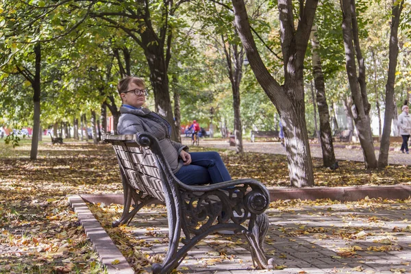 The young woman sits on a bench in the autumn park. Autumn sunny day — Stock Photo, Image