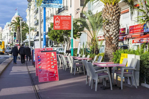 Niza, FRANCIA, en Enero 9, 2017. Las luces del sol Promenade des Anglais - el terraplén principal de la ciudad, uno de los más bellos del mundo, y istolik de café en la acera — Foto de Stock
