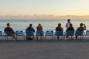 Güzel, Fransa, üzerinde 9 Ocak 2017. Günbatımı güneş gökyüzünde bulutlar ışıklar ve bir denizin dalgaları sörf. Üzerinde dolgu için dinlenme, bir Nice sembolleri mavi sandalye vardır