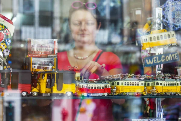 Lisbon, portugal, am 22. juni 2017. die junge attraktive frau betrachtet traditionelle souvenirs in einem Schaufenster des geschäfts hinter glas — Stockfoto